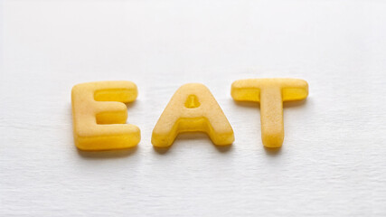 Naklejka premium The word EAT in yellow pasta letters on white, perfect for Italian restaurant logos, fun food typography, and playful culinary branding.