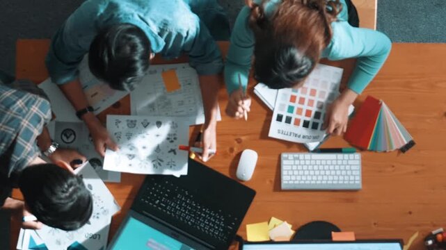 Top view of project manager writing idea while team joining meeting and talking about idea. Professional designer design logo while looking at color palette and writing idea down in paper. Symposium.