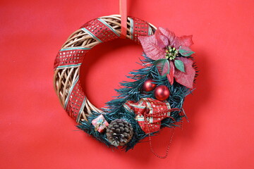 Christmas wreath with red bows, ornaments and pinecone hanging on bright red background for warm festive atmosphere.
