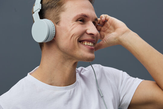 smiling young caucasian man wear white t-shirt listen music with headphones on gray background mental health and gadgets concept - Powered by Adobe