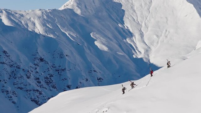 Aerial footage of four ski mountaineers carrying skis on their backs while climbing a snowy mountain ridge. Winter adventure in the Austrian Alps captured in cinematic 4K detail.