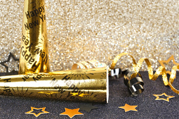 New Years Eve party decor on a twinkling gold and black background. Noisemakers, ribbon, confetti.