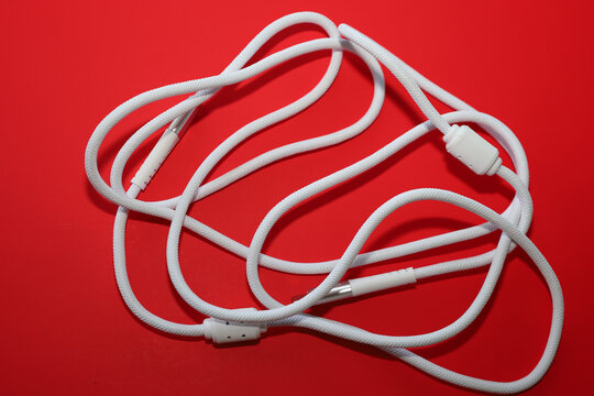 ​A whiteType-C  Type-C cable with a fabric braid is tangled lying in loops on a saturated red background, creating a bright color contrast.