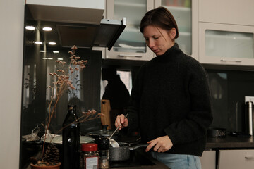 A woman cooks in a cozy kitchen, stirring food in a pot under soft lights and creating a warm, calm everyday atmosphere.