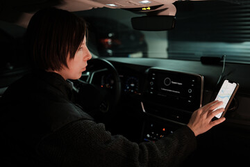 A woman in a parked car touches her smartphone mounted near the dashboard, preparing navigation before driving. The scene reflects modern travel habits and digital mobility.