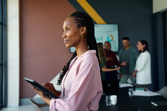 Thoughtful black young businesswoman using tablet in office with colleagues in background