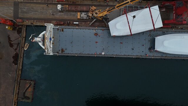 Industrial footage of ship loading operations at a shipyard port. Workers and heavy machinery handle cargo and marine equipment, showing maritime logistics, ship maintenance, and port activities. Idea