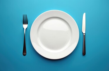 White plate, fork, and knife arranged on blue backdrop. Minimalist setup for meal or fasting theme. Clean design, ready for food content or graphic.
