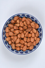 An overhead view of a small, patterned blue and white bowl filled with shelled, roasted hazelnuts on a white background