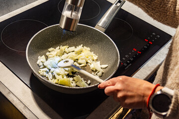 Person adding seasoning to onions in frying pan