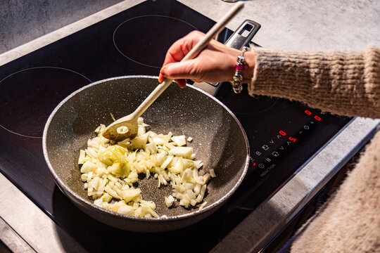 Person stirring chopped onions in pan.