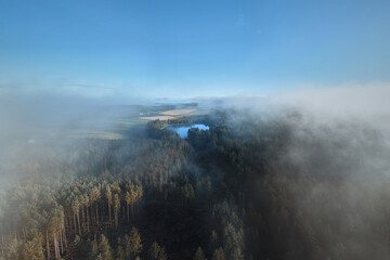 Aerial view of a mist-covered forest and a small lake in West Lothian, Scotland. Morning fog drifting over the treetops creates a serene and atmospheric landscape. Beecraigs Country Park, Scotland