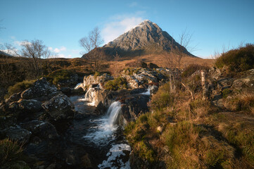 Scenic view of Buachaille Etive Mor in Glen Coe, Scotland, with a small waterfall flowing over rocks on a clear day. Natural landscape, mountain scenery and freshwater stream. 