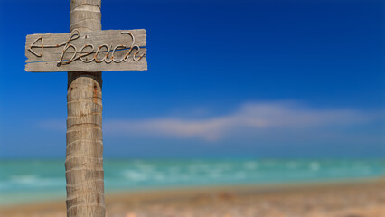 Signpost to the beach made from manila rope on old wooden board stick on coconut pole with blurred beach and blue sky background, Image for summer or travel theme with copy space and selective focus.