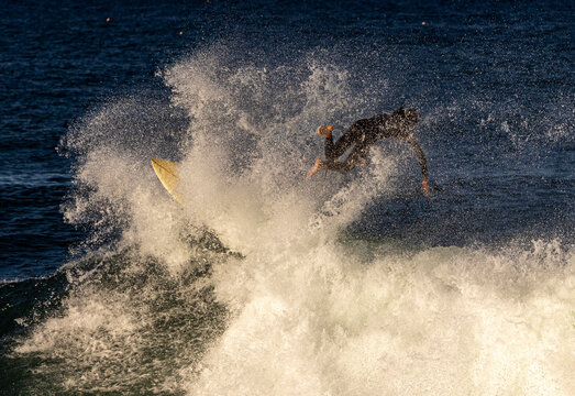 A surfer wearing a wetsuit wiping out on the lip of a wave