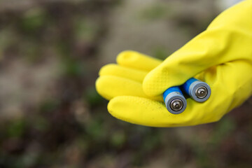 Close-up of a volunteer wearing yellow gloves holding discarded batteries collected on a polluted beach. Environmental cleanup, toxic waste, coastline protection and eco awareness.
