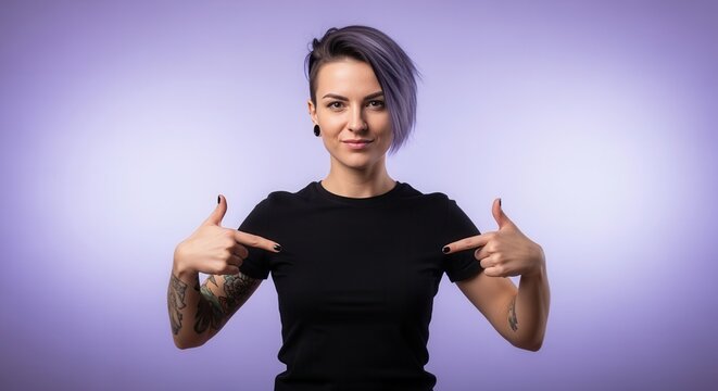 Confident woman with purple hair pointing at her blank black t-shirt. T-shirt mockup for custom design placement. Alternative model with tattoos on a purple background