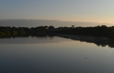 Wide tranquil lake under warm sunset sky creates calm evening mood with gentle reflections. Soft golden light spreads across quiet lake during sunset,