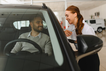 Saleswoman talking to customer admiring new vehicle in showroom