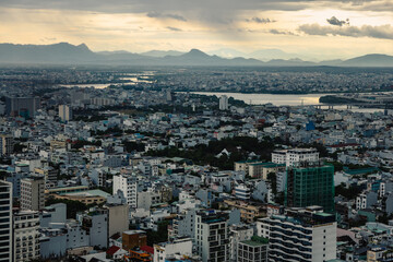 Fototapeta premium A moody aerial view of Da Nang’s iconic Dragon Bridge, surrounded by dense city buildings and a large construction site under foggy weather.