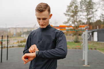 caucasian man checks smartwatch during outdoor workout wearing black training jacket, focused expression