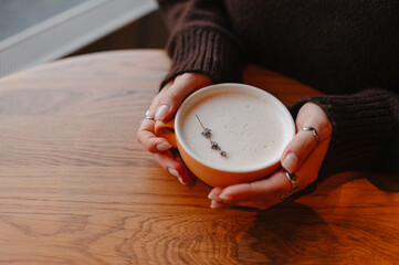 warm cappuccino held in hands, mindful studio break by designer wearing chunky sweater; three...
