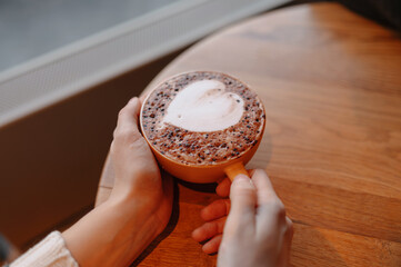 latte art heart in hands, cozy morning ritual for freelance writer holding ceramic mug near window;...