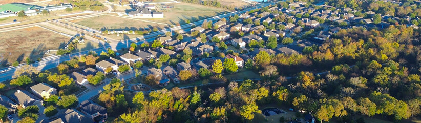 Panorama aerial farm, ranch, suburban homes in Lantana, Texas, bordered by wooded area fall foliage, visible pools, undeveloped land beyond, showcases residential growth and seasonal contrast