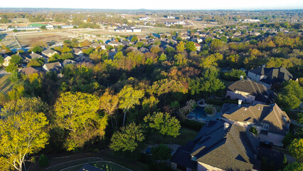 Farm background from lush green suburban homes in Lantana, Texas, wooded area fall foliage, visible pools, garages, undeveloped land beyond, illustrating residential growth, seasonal contrast
