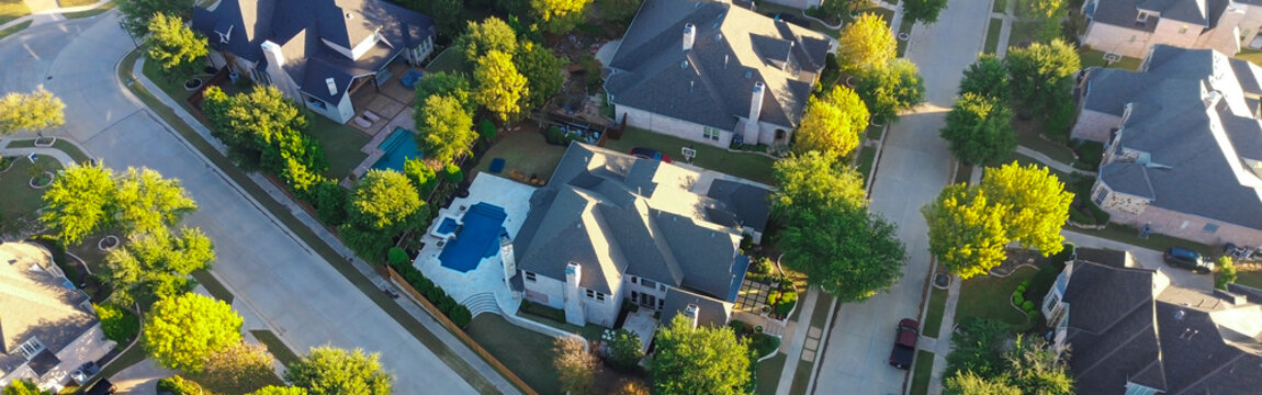 Panorama aerial densely packed homes in Lantana, Texas, arranged in grid with curved streets and cul-de-sacs, features varied rooflines, backyard pools, and tree-lined roads in green environment