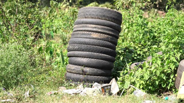 Old used car tires surrounded by overgrown grass near a road.
