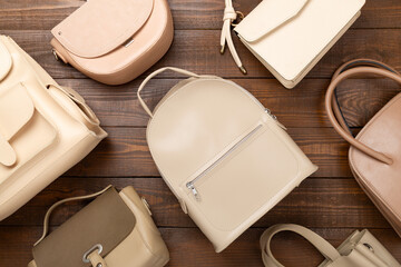 Fashionable beige colored women's bags on wooden background, top view