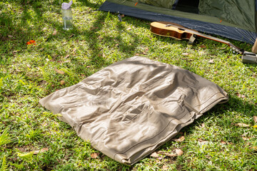Camping scene with deflated mattress, tent, guitar, water bottle, and accessory on grassy ground