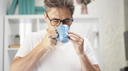 Uncombed middle aged man drinking morning coffee at home.
