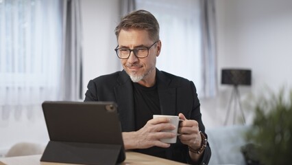 Businessman working with tablet computer in home office. Happy middle aged, mid adult, mature age man smiling. Entrepreneur sitting at desk, managing business online.