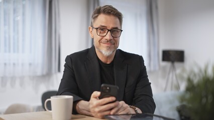 Businessman at home, using phone, checking newsfeed. Home office, browsing internet. Portrait of happy, mature age, middle age, mid adult man in 50s, smiling.