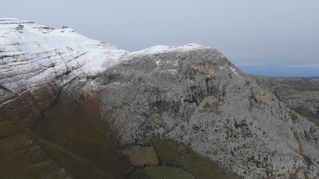 Snow-covered mountains overlook a river valley, Cantabria - Here is a revised description that meets the critical rules: A mountainous landscape shows snow-covered areas in the background under a.