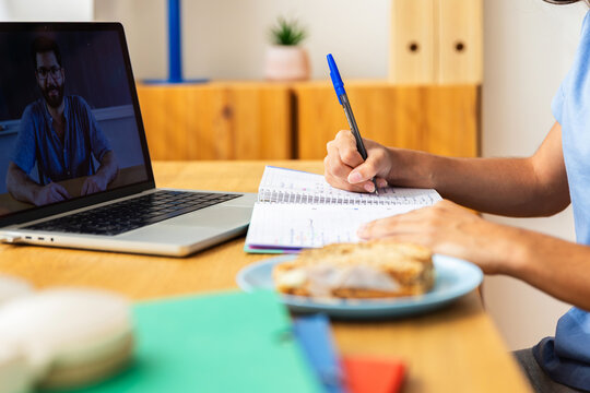 Teenage student girl taking notes while participating in an online class on her laptop, focused on learning from home at her desk - Powered by Adobe