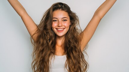 A young woman with long, flowing hair is smiling broadly while raising her arms in the air. The background is simple and bright, creating a joyful atmosphere.