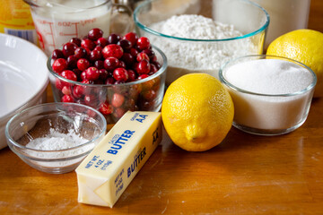 Homemade cranberry lemon cake ingredients: flour, butter, fresh cranberries, and lemon on a rustic dark wood cutting board. Natural light.