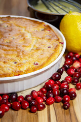 Whole baked cranberry cake with lemon glaze ingredients: saucepan, whisk, and fresh lemon slices. Rustic homemade holiday dessert.