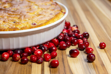 Rustic close-up of a freshly baked cranberry cake showing the golden, cracked crust and edge of the dish on a dark wood board. Cozy homemade food.