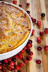 Rustic close-up of a freshly baked cranberry cake showing the golden, cracked crust and edge of the dish on a dark wood board. Cozy homemade food.