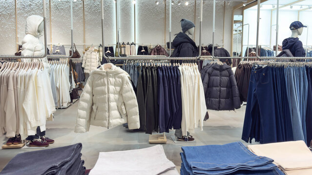 Modern clothing store interior with neatly arranged jackets, sweaters, hoodies denim on racks and shelves. Neutral colors, clean layout mannequins create stylish, organized retail shopping atmosphere
