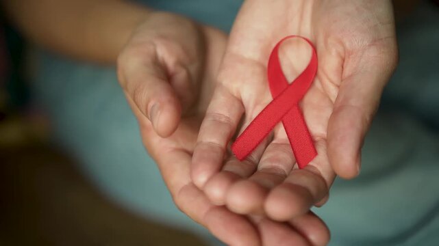 Female hand presenting red satin ribbon for HIV AIDS awareness, symbolizing December remembrance and support for medical research.