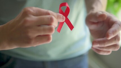 Close-up of male hand transferring red awareness ribbon to female hand symbolizing shared support for HIV AIDS awareness and solidarity.
