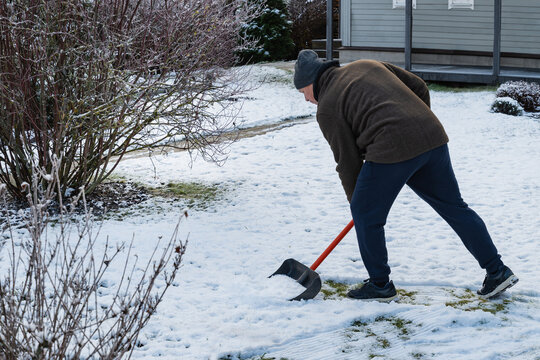Senior man clearing snow in backyard with shovel, performing winter chores and maintaining clean pathways in cold weather. Winter Yard Work Snow Removal and Garden Maintenance