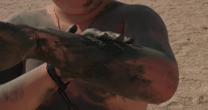 A child rubs himself with blue clay A boy enjoys a spa treatment on a sunny beach applying therapeutic blue clay rich in minerals to his hands and body for a healthy and fun outdoor skincare routine.