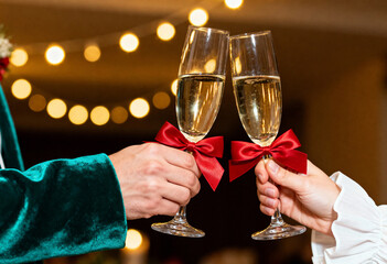 Close-up of a couple making a toast with champagne glasses. Festive red bows on flutes for a Christmas or New Year's Eve celebration