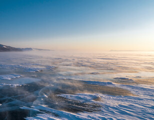 Fototapeta premium Windblown snow drifting across wide frozen winter plain under sunlight